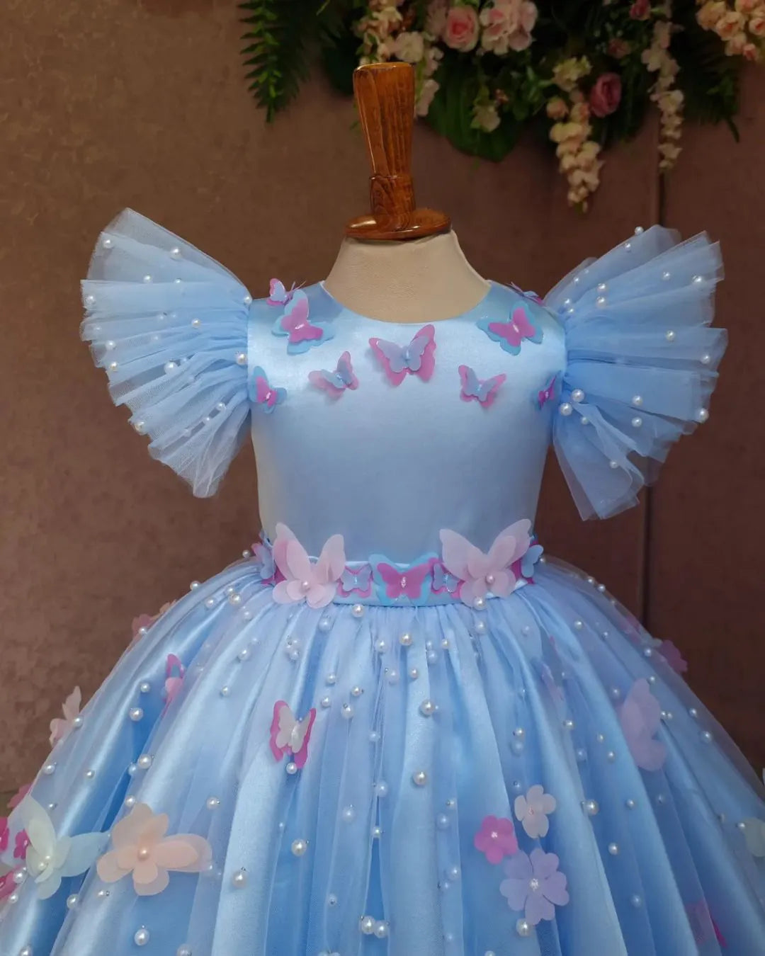 Close-up of pearl and floral embellishments on pastel blue butterfly-themed dress.