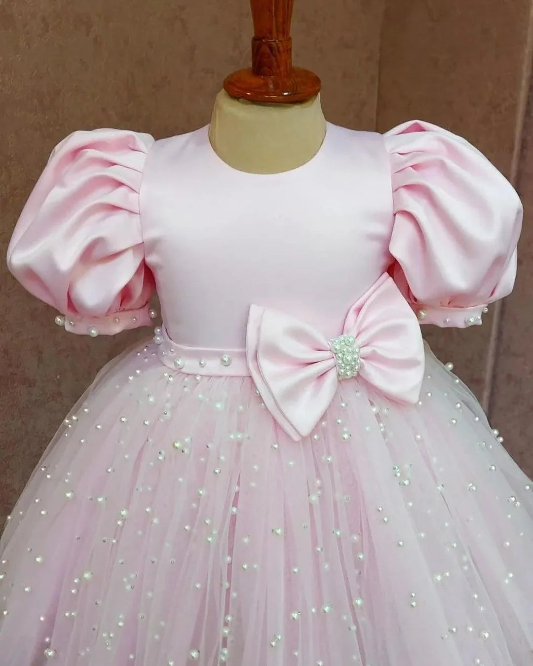 Close view of a pink formal dress with puff sleeves, highlighting the smooth satin finish and luxurious design.