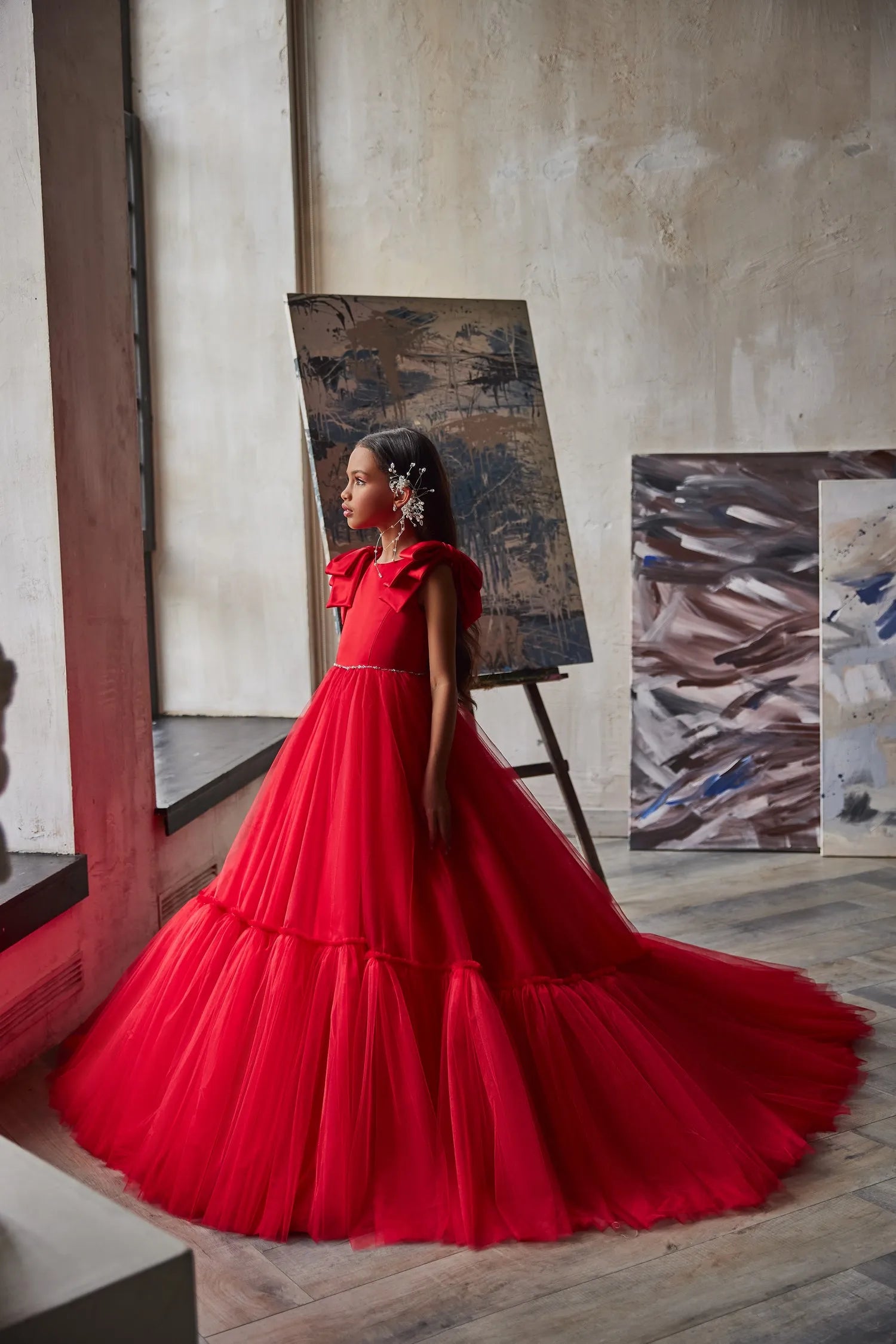 Girl wearing the Ruby Reverie red flower girl dress, radiating joy at a formal event with a beaming smile.