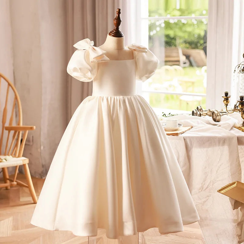 Side view of an elegant ivory puff sleeve gown for young girls, highlighting the dress’s luxurious satin fabric and flowing shape.