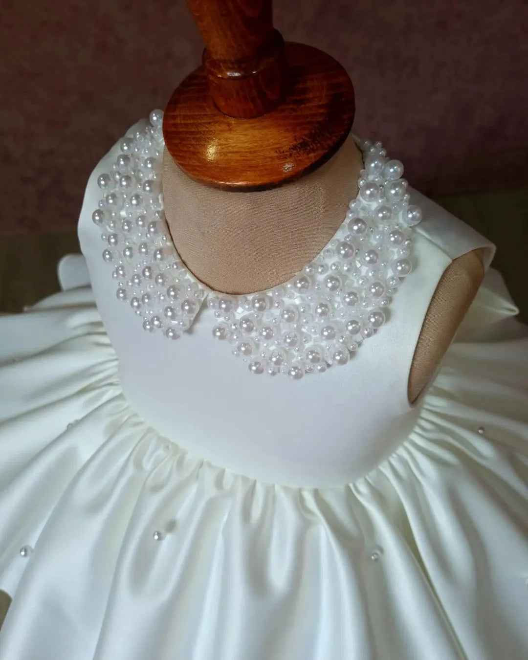 Close-up of the pearl-embellished collar on a white satin dress, showing intricate detail and luxury.