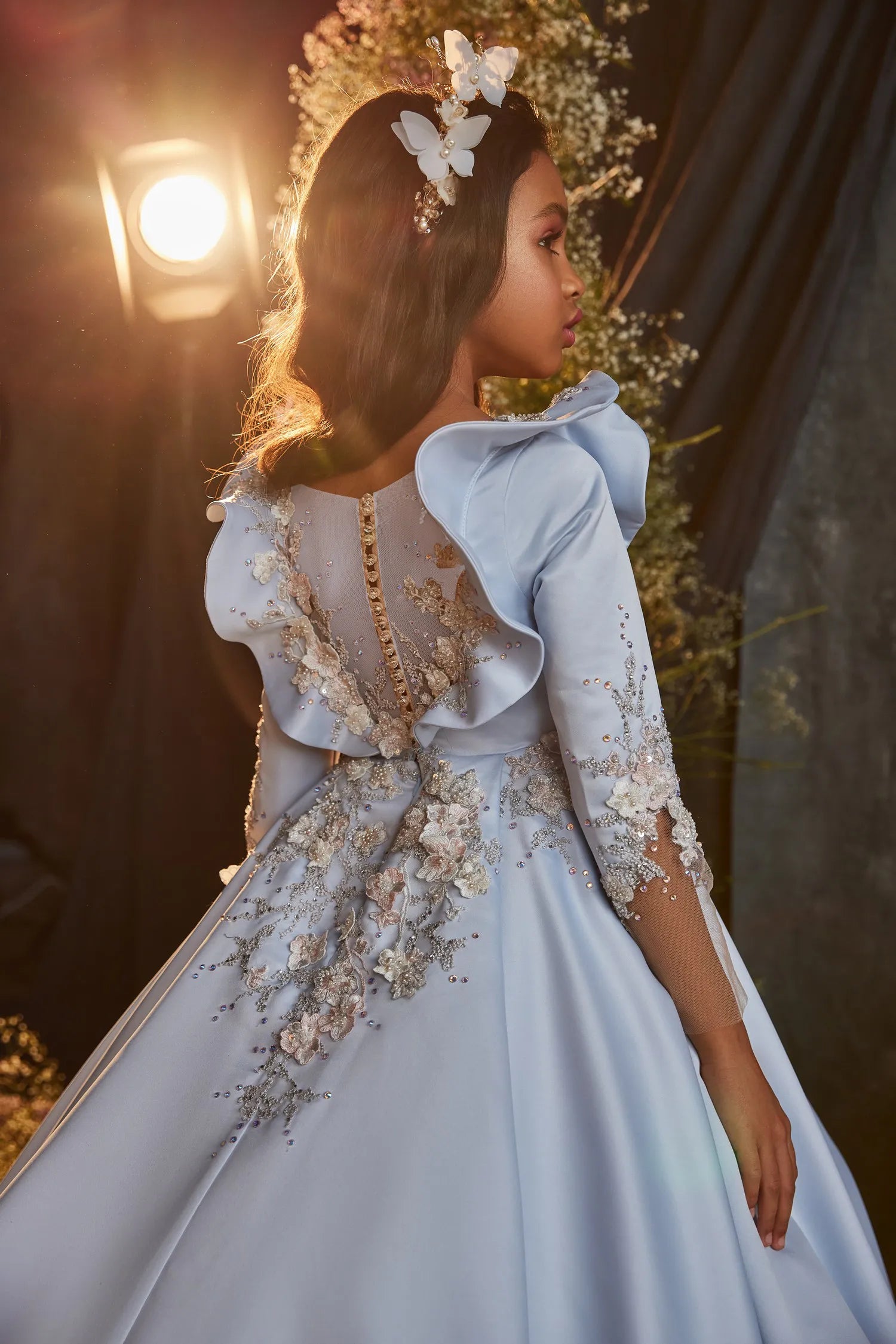 Side angle of a vintage-style girls' satin gown in sky blue, featuring intricate lacework and ruffled sleeve accents.